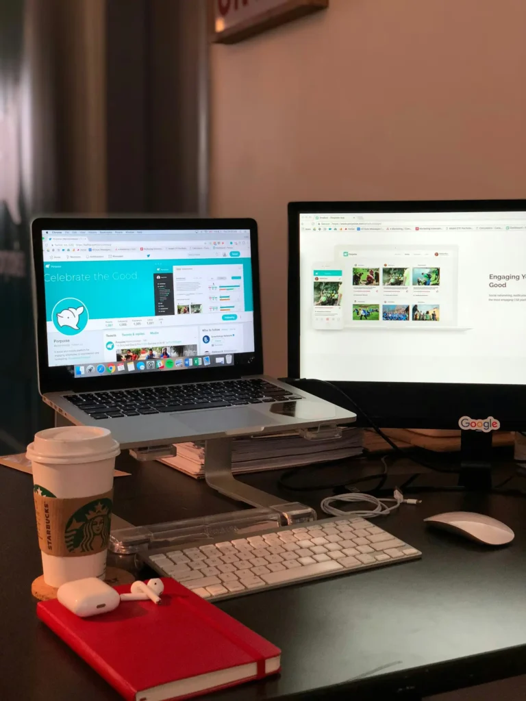 Heimarbeitsplatz mit Dual-Monitor-Setup, Starbucks-Kaffeebecher, AirPods, rotem Notizbuch und sichtbaren Social-Media-Inhalten auf dem Bildschirm – modernes Setup für Content-Erstellung und Social-Media-Management