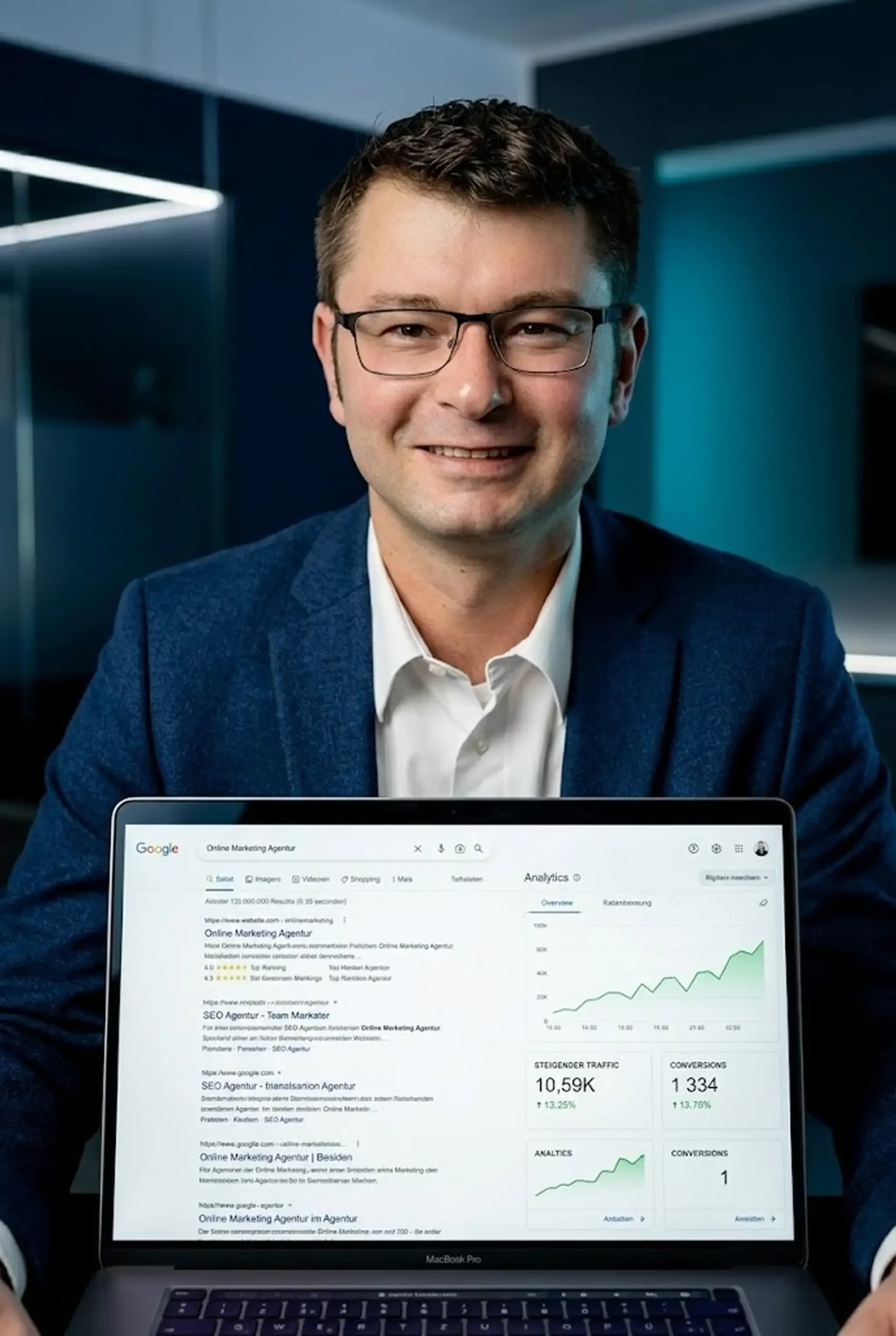 Dennis Klein von Klein WebCraft hält ein MacBook mit sichtbaren Google-Suchergebnissen und Google Analytics-Dashboard mit 10.590 Sitzungen und 1.334 Conversions – Ergebnis professioneller SEO-Optimierung