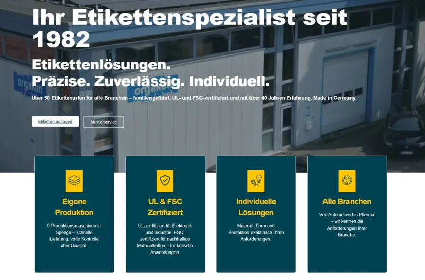Screenshot der orgakett.de WooCommerce-Website: Industriegebäude-Fassade mit orgakett-Firmenschild als Hero-Hintergrund, Headline Ihr Etikettenspezialist seit 1982, Subheadline Etikettenlösungen Präzise Zuverlässig Individuell und vier Leistungskarten
